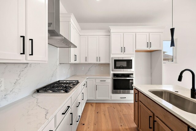 kitchen with stainless steel appliances, wall chimney range hood, decorative light fixtures, and white cabinets