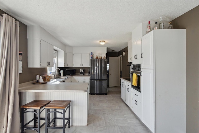 kitchen with white cabinets, stainless steel fridge, sink, a textured ceiling, and a breakfast bar