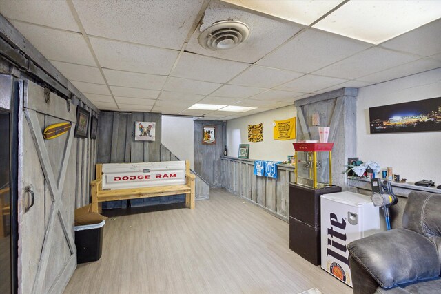 basement featuring a paneled ceiling, wood walls, and hardwood / wood-style floors