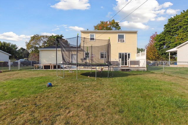 rear view of property with a trampoline, a deck, and a lawn