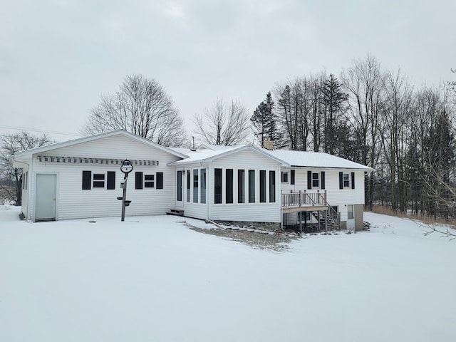 snow covered rear of property featuring a sunroom