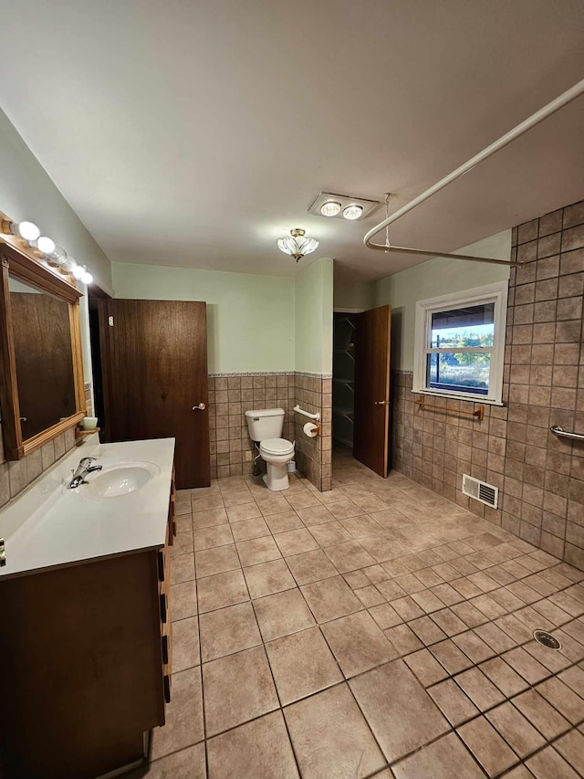 bathroom with tile walls, vanity, toilet, and tile patterned flooring