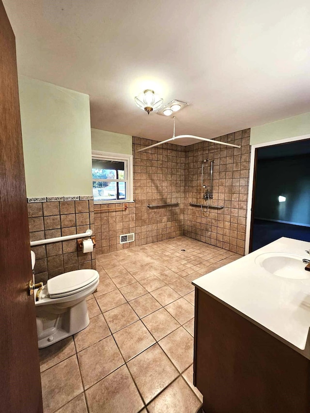 bathroom with toilet, tile walls, tiled shower, vanity, and tile patterned flooring