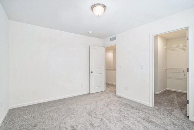 unfurnished bedroom featuring a spacious closet, a closet, and light colored carpet