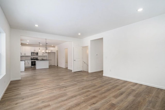 unfurnished living room featuring an inviting chandelier and light hardwood / wood-style flooring