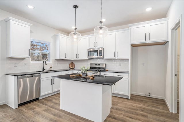 kitchen with pendant lighting, sink, appliances with stainless steel finishes, a kitchen island, and white cabinetry