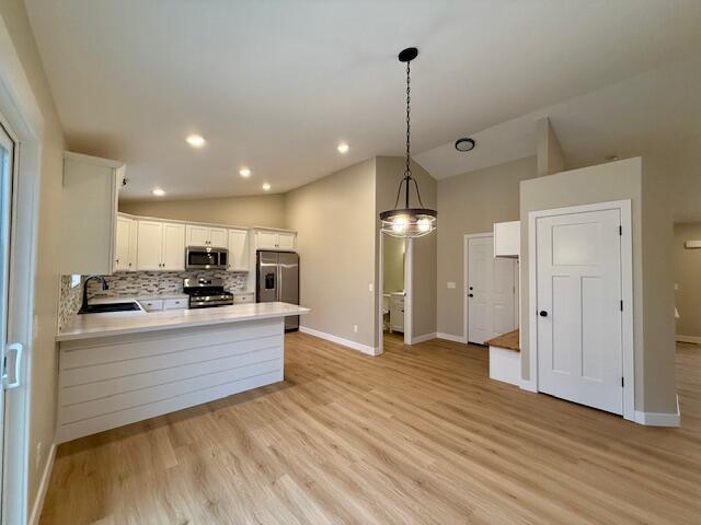 kitchen with pendant lighting, vaulted ceiling, white cabinetry, kitchen peninsula, and stainless steel appliances