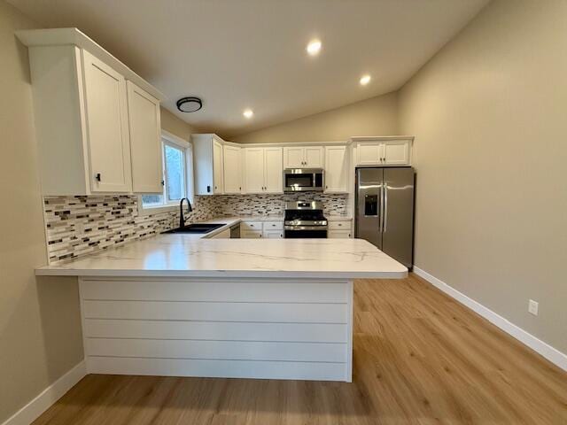 kitchen with kitchen peninsula, appliances with stainless steel finishes, vaulted ceiling, sink, and white cabinetry