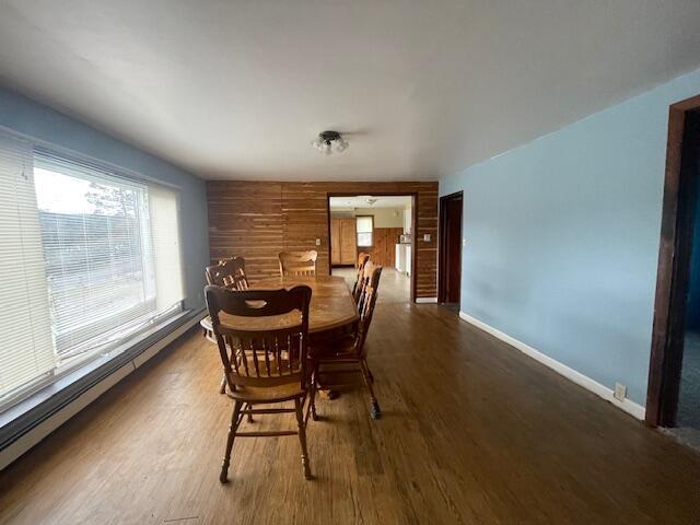 dining area featuring dark hardwood / wood-style flooring, baseboard heating, and wooden walls