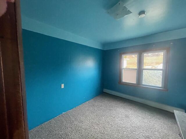 carpeted empty room with a baseboard heating unit