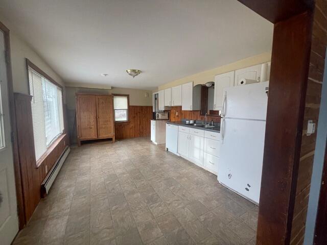 kitchen featuring sink, baseboard heating, wood walls, white fridge, and white cabinets