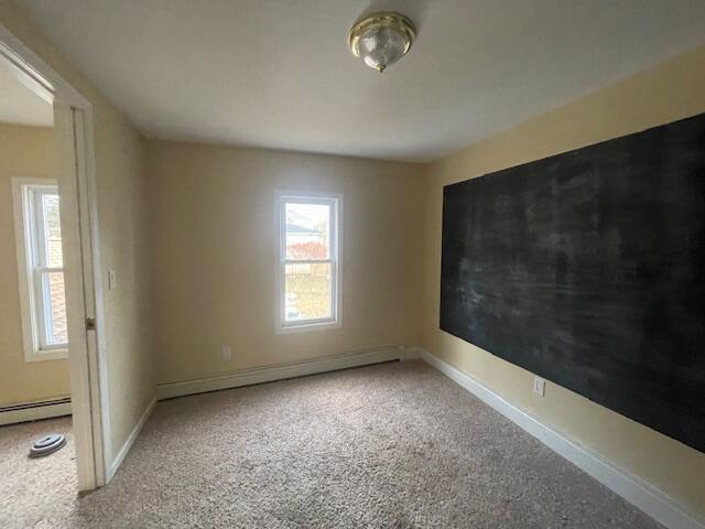 unfurnished room featuring carpet floors and a baseboard heating unit