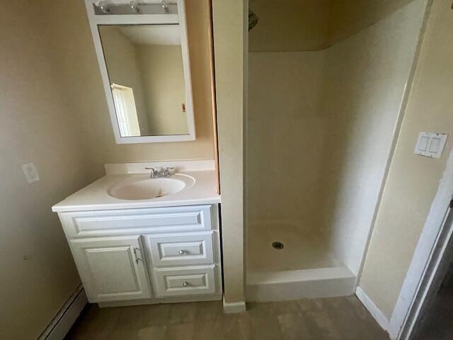 bathroom with walk in shower, vanity, and baseboard heating