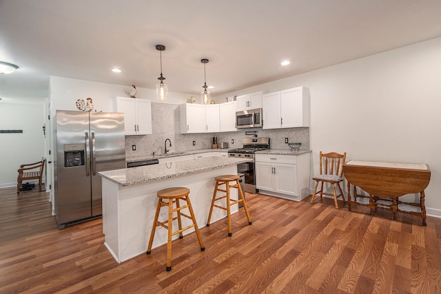 kitchen featuring white cabinets, hardwood / wood-style flooring, appliances with stainless steel finishes, a center island, and decorative backsplash