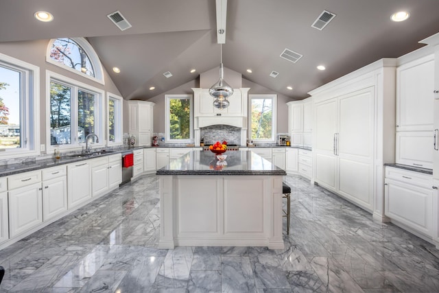 kitchen featuring white cabinets, sink, a kitchen island, backsplash, and dark stone countertops