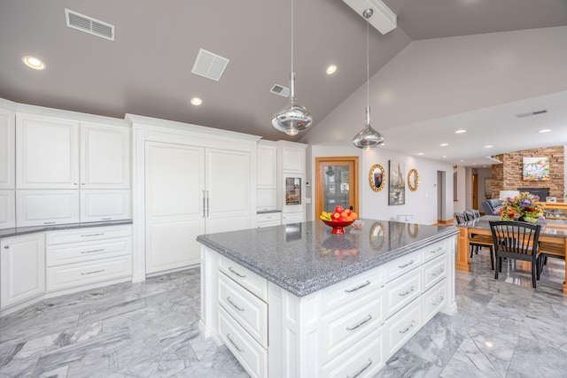 kitchen with a kitchen island, white cabinets, a fireplace, hanging light fixtures, and vaulted ceiling