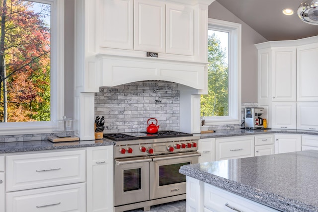 kitchen featuring range with two ovens, dark stone countertops, white cabinets, and a wealth of natural light