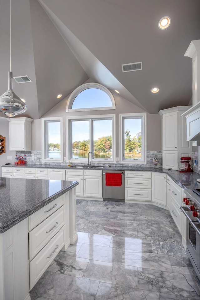 kitchen featuring white cabinets, backsplash, appliances with stainless steel finishes, dark stone counters, and vaulted ceiling