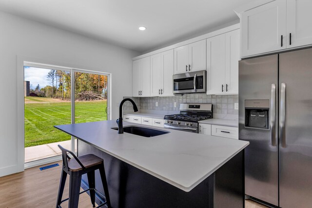 kitchen featuring light wood-type flooring, a kitchen island with sink, stainless steel appliances, white cabinets, and sink