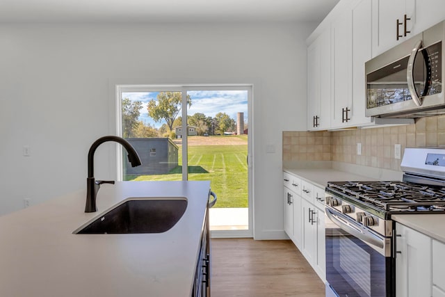 kitchen with decorative backsplash, stainless steel appliances, white cabinets, sink, and light hardwood / wood-style floors