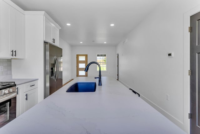 kitchen featuring light stone counters, white cabinets, sink, stainless steel appliances, and decorative backsplash