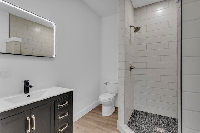 bathroom featuring a tile shower, hardwood / wood-style flooring, vanity, and toilet