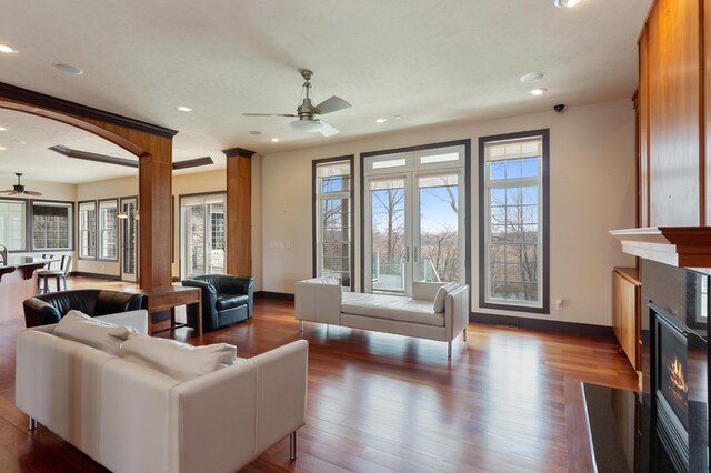 living room featuring ceiling fan, ornate columns, and dark wood-type flooring