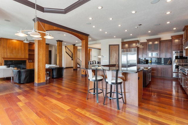 kitchen featuring a center island, dark hardwood / wood-style floors, hanging light fixtures, decorative columns, and built in appliances