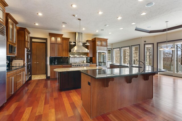 kitchen featuring pendant lighting, wall chimney range hood, and a spacious island