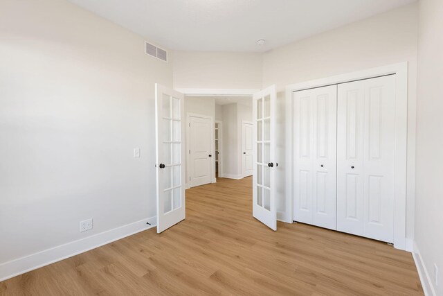 unfurnished bedroom with a closet, french doors, and light wood-type flooring