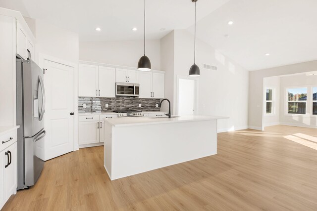 kitchen featuring an island with sink, white cabinetry, light hardwood / wood-style floors, stainless steel appliances, and pendant lighting