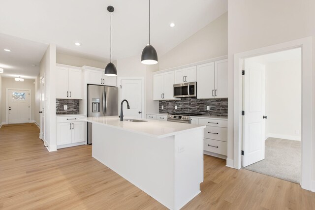 kitchen featuring a kitchen island with sink, hanging light fixtures, white cabinets, light wood-type flooring, and appliances with stainless steel finishes