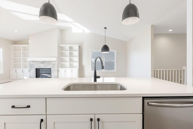 kitchen with sink, vaulted ceiling, decorative light fixtures, stainless steel dishwasher, and white cabinetry