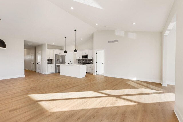 unfurnished living room with sink, high vaulted ceiling, and light wood-type flooring