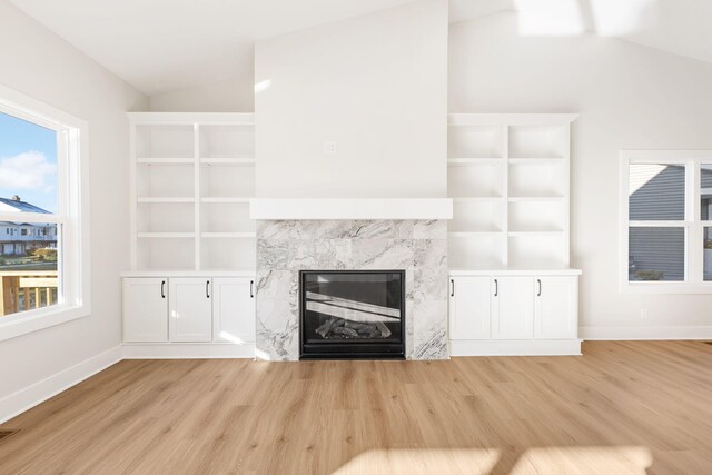 unfurnished living room with vaulted ceiling, a fireplace, and light wood-type flooring