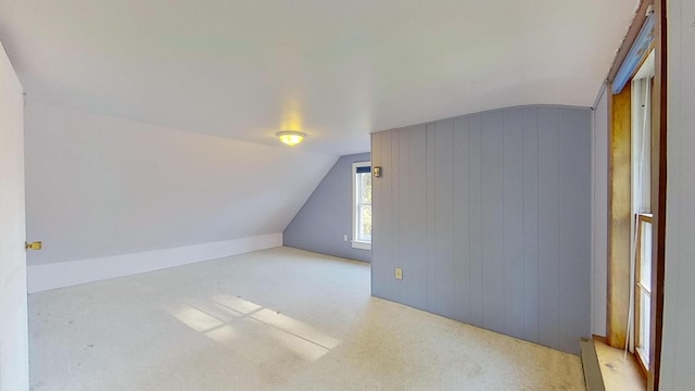 additional living space with light colored carpet, wooden walls, and vaulted ceiling