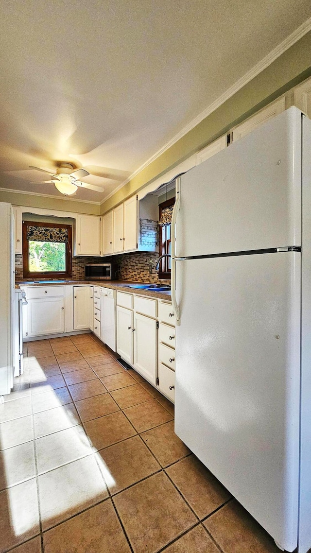 kitchen with white appliances, light tile patterned flooring, backsplash, white cabinets, and ornamental molding