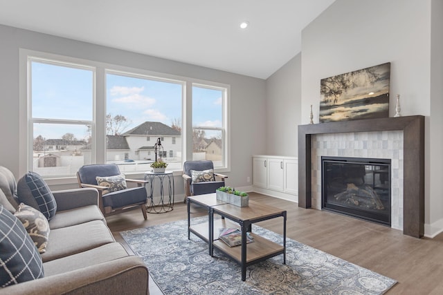 living room with vaulted ceiling, a tiled fireplace, wood finished floors, and baseboards