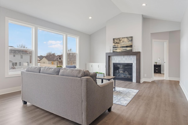 living room with lofted ceiling, recessed lighting, wood finished floors, baseboards, and a tiled fireplace