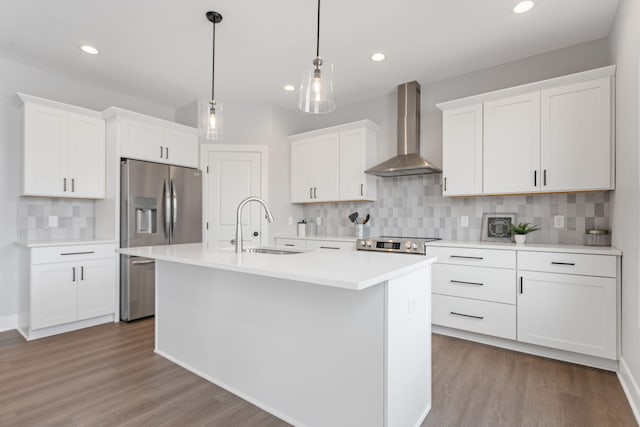 kitchen with stainless steel appliances, light countertops, white cabinets, a sink, and wall chimney exhaust hood