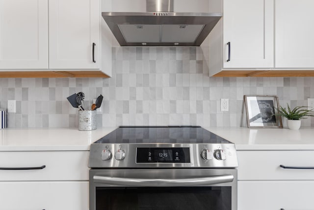 kitchen with wall chimney range hood, stainless steel electric stove, white cabinets, and light countertops