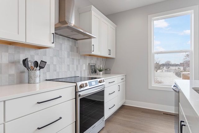 kitchen with stainless steel electric stove, white cabinetry, baseboards, decorative backsplash, and wall chimney exhaust hood