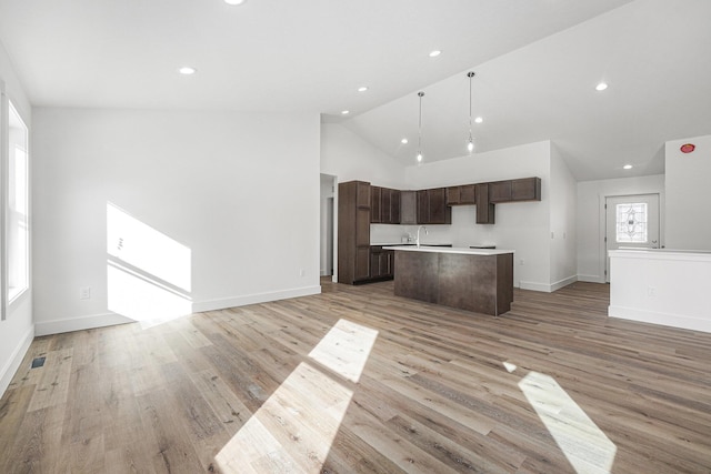 kitchen featuring pendant lighting, dark brown cabinets, high vaulted ceiling, light hardwood / wood-style floors, and a center island with sink