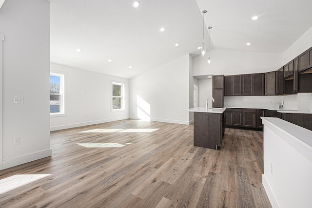 kitchen with hanging light fixtures, light wood-type flooring, a center island with sink, and dark brown cabinetry