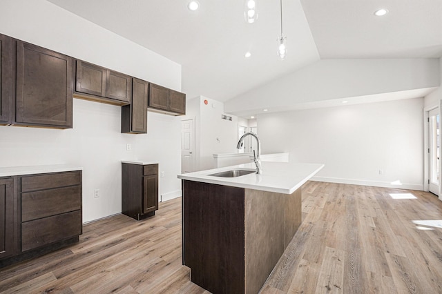 kitchen featuring vaulted ceiling, decorative light fixtures, sink, a kitchen island with sink, and dark brown cabinets