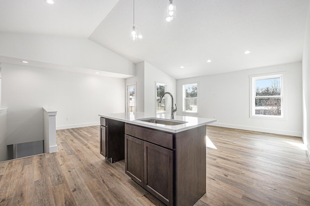 kitchen with sink, light hardwood / wood-style flooring, an island with sink, decorative light fixtures, and vaulted ceiling