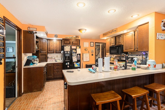 kitchen with kitchen peninsula, black appliances, a breakfast bar area, and a textured ceiling