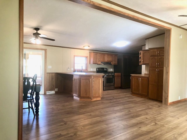 kitchen featuring wooden walls, ceiling fan, wood-type flooring, stainless steel gas stove, and kitchen peninsula