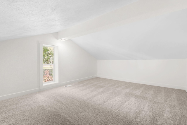 bonus room with a textured ceiling, vaulted ceiling with beams, and carpet flooring