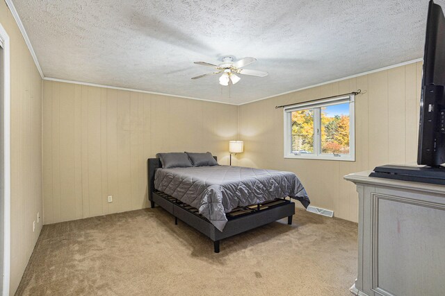 bedroom featuring a textured ceiling, light colored carpet, wooden walls, and ceiling fan